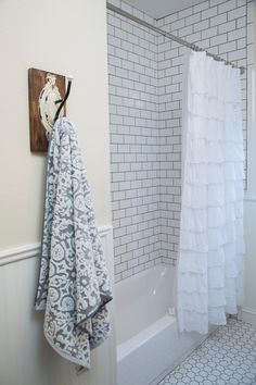 a bathroom with white and gray towels hanging on the shower curtain, next to a bathtub