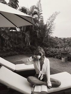 a woman sitting on top of a white couch next to an open book and umbrella