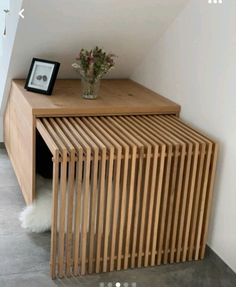 a wooden table with a vase on top of it next to a white wall and floor