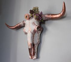 a cow's skull with flowers on it is mounted to the wall in front of a gray wall