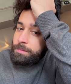 a man with long hair and beard wearing a gray sweater is looking at the camera