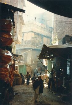 people walking through an alleyway in the city with buildings on either side and one person carrying something