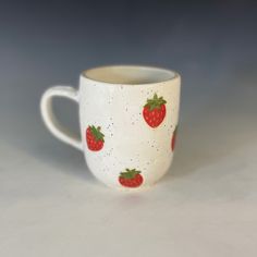 a white cup with strawberries on it sitting on a table next to a gray background