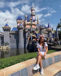 a woman sitting on the edge of a stone wall in front of a disney castle