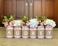 four mason jars with flowers in them sitting on the ground next to a door way