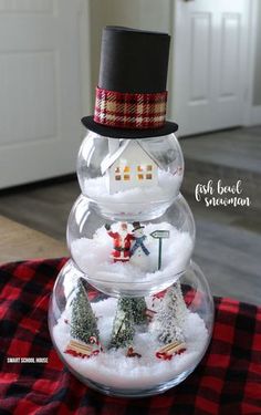 a snowman is sitting on top of a glass bowl filled with snow and trees