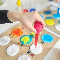 a child's hand is holding a red paintbrush and painting circles on paper