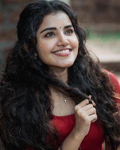 a woman with long black hair smiling at the camera while wearing a red dress and holding her hand on her shoulder