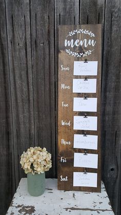 a wooden sign sitting on top of a table next to a vase with flowers in it