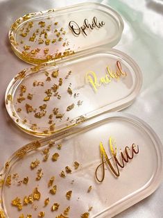 three clear trays with gold confetti and name tags on them sitting on a white surface