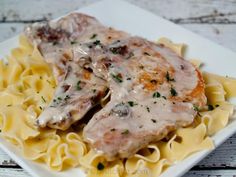 two pieces of meat and pasta on a white plate with parmesan cheese sauce