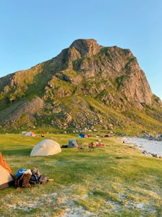 there are many tents set up on the grass by the water with mountains in the background