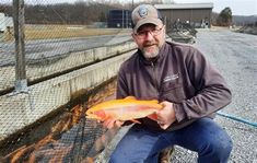 a man holding a fish in front of a fence