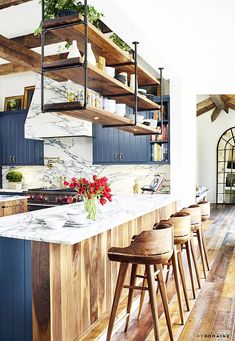 a kitchen with blue cabinets and marble counter tops, wooden bar stools and open shelving