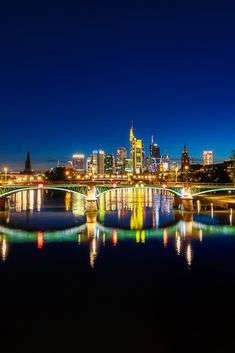 the city skyline is lit up at night with lights reflecting on the water and bridge