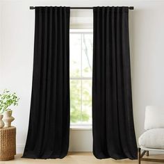 the black curtains are hanging in front of a window with a white chair and potted plant