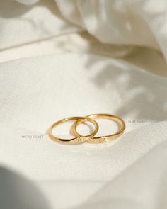 two gold wedding rings sitting on top of a white cloth covered tablecloth, close up