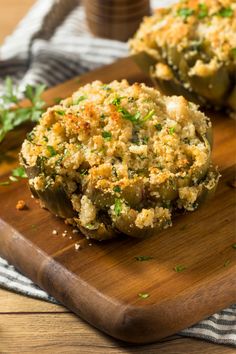 two stuffed peppers on a cutting board with parsley sprinkled on top and another item in the background