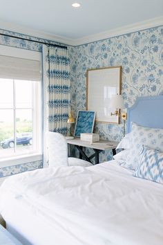 a bedroom with blue and white floral wallpaper, a large bed, and a desk in front of a window