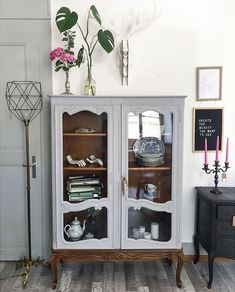 an old china cabinet with glass doors and flowers on the top shelf in a living room