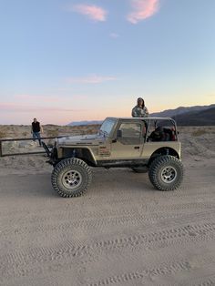 two people standing on top of a truck in the desert, with one person looking over the bed