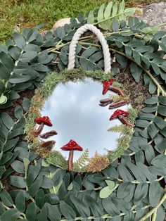 a circular mirror with red mushrooms and leaves on the bottom is surrounded by greenery