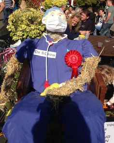 a scarecrow sitting in a chair with a red ribbon around his neck and head