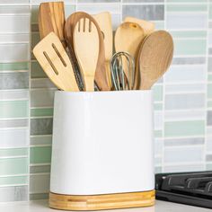 wooden utensils and spoons in a white container on a counter top next to a stove