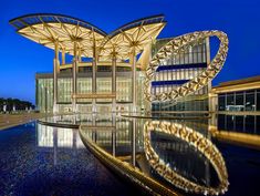 an artistic building is reflected in the water at night with blue sky and clouds behind it