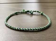 a green and white braided bracelet sitting on top of a wooden table