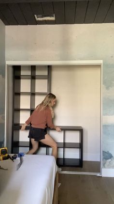 a woman standing on top of a bed next to a book shelf in a room