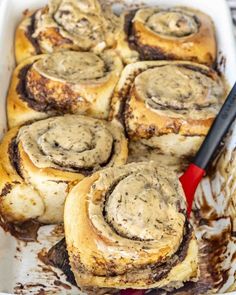 cinnamon rolls in a baking dish with a spatula on the side and chocolate sauce drizzled over them