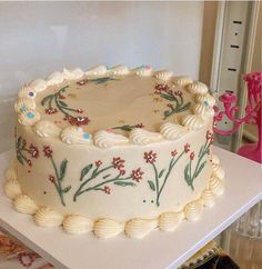 a decorated cake sitting on top of a white table next to a pink vase with flowers