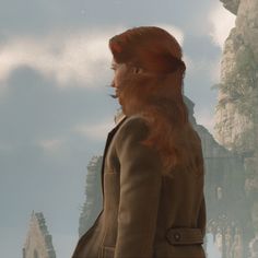 a woman with long red hair standing in front of a mountain and looking into the distance