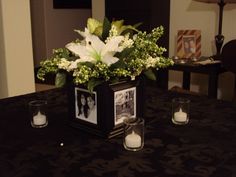 a vase with white flowers and candles on a black table cloth covered dining room table