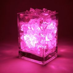 an ice cube with pink lights in the middle on a dark surface, it appears to be filled with chunks of ice