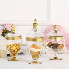 three glass containers filled with food on top of a white table next to pink roses