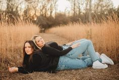 two women are laying on the ground in front of some tall grass and trees with their arms around each other