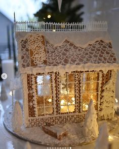 a small white gingerbread house on a plate with christmas lights in the window behind it