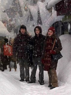 three people are standing in the snow near a train station and trees with falling snow