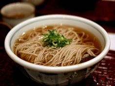 a white bowl filled with noodle soup on top of a wooden table