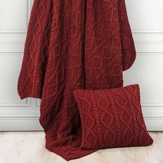 a red blanket and pillow sitting on top of a wooden floor next to a white wall