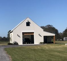 a large white barn with a car parked in the front door and another building behind it