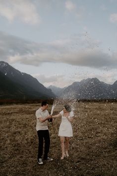 a man and woman standing in an open field with snow falling from the sky behind them