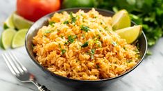 mexican rice in a bowl with limes, tomatoes and cilantro on the side