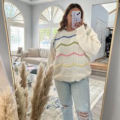 a woman taking a selfie in front of a mirror wearing ripped jeans and a sweater