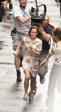 a group of people running in the rain with a camera on their shoulder and one person holding an umbrella