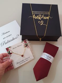 a person holding a necklace next to a box with a card and tie on it