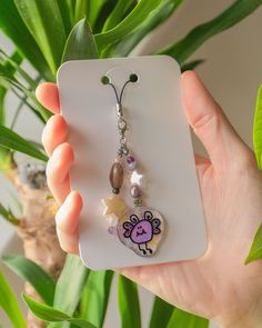 a hand holding a cell phone charm with a cartoon character on it and beads hanging from the back