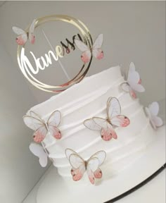 a white cake with pink butterflies on it and the name annna written in gold